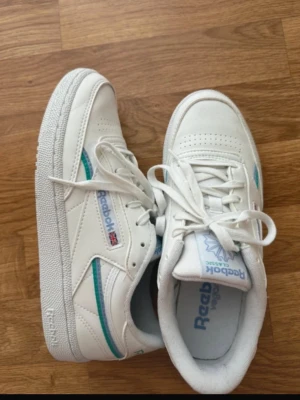 Vita Reebok sneakers club 85 - Säljer ett par vita Reebok sneakers modellen club 85 med klassisk låg profil och rund tå. Strl 38, i princip i nyskick, använda 2 gånger varav lite smutsig sula