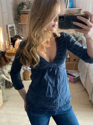 Mörkblå blus med v-ringning och knyt - Supersnygg mörkblå blus med djup v-ringning och dekorativa detaljer framtill. Blusen har trekvartsärm och knytband i ryggen för en fin passform. Perfekt till jeans och enkel att styla upp eller ner. Materialet känns mjukt och lätt.