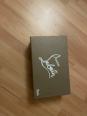 Christian Louboutin svarta sneakers - Säljer ett par svarta sneakers från Christian Louboutin med klassisk röd sula och coola svarta nitar på tån. Skorna har snörning och är tillverkade i mocka för en lyxig känsla. Kommer med originalkartong, dustbag och äkthetskort.