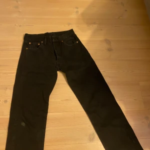 Svarta Levi's 501 jeans straight fit - Klassiska svarta Levi's 501 jeans med rak passform och fem fickor. Jeansen har knappgylf och är tillverkade i slitstark bomull. Perfekta för dig som gillar tidlös stil och vill ha ett par riktigt schyssta jeans i garderoben.