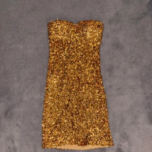 Guldig paljettklänning från Man Tian - Säljer en glittrig guldig kortklänning från Man Tian, täckt med paljetter. Klänningen är axelbandslös och har en figurnära passform. Använt 1 gång på nyår!💕så fint skick! 