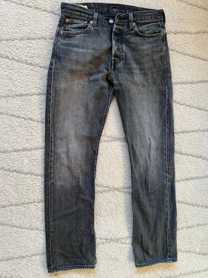 Levi's 501 svarta jeans straight fit - Svarta Levi's 501 jeans med klassisk femficksdesign och raka ben. Jeansen har en snygg tvättad look och är tillverkade i slitstarkt bomullsjeans. Perfekta för dig som gillar en tidlös och avslappnad stil.  Storleken är 30/32