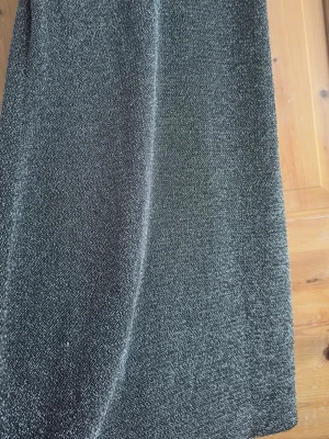 Glittrig svart kortklänning - Säljer en glittrig svart kortklänning med tunna axelband och rak passform. Klänningen har en snygg v-ringning och skimrar i ljuset, perfekt för dig som vill sticka ut. Materialet känns mjukt och följsamt mot kroppen.