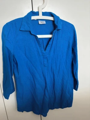 Blå skjorta - Säljer en blå henley-skjorta från bpc bonprix collection i storlek 36. Skjortan har en klassisk krage, v-ringad hals och trekvartsärm. Materialet är linne vilket gör den skön och luftig. Perfekt för dig som gillar enkel och stilren design.