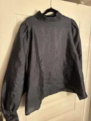 Mörkgrå lös blus från Stockh LM - En mörkgrå blus från Stockh LM med lös passform och knappar vid ärmslutet och vid nacken.