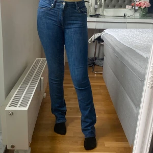 Mörkblå bootcut jeans med medel hög midja - Snygga mörkblå jeans med hög midja och klassisk rak passform. Jeansen har fem fickor, dragkedja och knapp framtill. Perfekta till sneakers eller boots och funkar året runt. Materialet är robust denim som håller formen. 