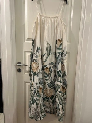 Blommig långklänning från H&M - Luftig långklänning från H&M i linneblandning med smala axelband och vackert blommönster i grönt och beige på vit botten. Perfekt för varma dagar och ger en chill sommarkänsla. Klänningen har en loose passform och är superenkel att styla.