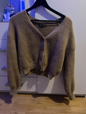 Beige ribbad kofta med knappar - Snygg beige ribbad kofta med v-ringning och stora dekorativa knappar framtill. Modellen är croppad och har långa ärmar med breda muddar. Storlek M men är ganska kort. Lånad bild men de är bara att skriva för fler bilder 