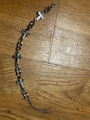 Silverfärgat armband med kors - Snyggt armband i silverfärgad metall med flera kors som detaljer. Kedjan har större länkar och ett justerbart spänne för perfekt passform. Perfekt accessoar för dig som gillar edgy och stilrena smycken.