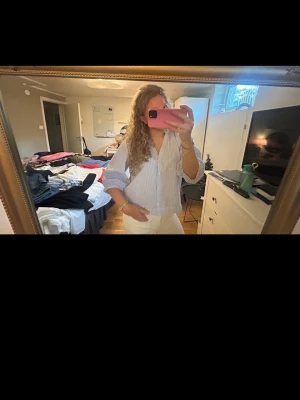 Blårandig skjorta med v-ringning - Säljer en blårandig skjorta med v-ringning och långa ärmar. Skjortan har en avslappnad passform och är tillverkad i ett lätt material, perfekt för vår och sommar. Klassisk look med knappar framtill och uppvikta ärmslut.