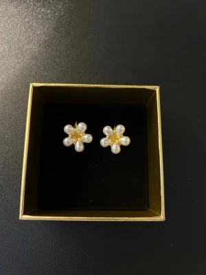 Blomformade örhängen med pärlor - Supersöta örhängen i form av blommor med vita pärlor som kronblad och guldfärgad metall i mitten och krok.
