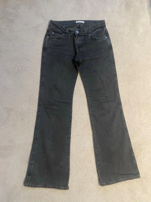 Svarta straight jeans från Gina Tricot - Snygga svarta raka jeans från Gina Tricot med klassisk femficksmodell och silverfärgade knappar på bakfickorna. Jeansen har en något utsvängd passform och är tillverkade i mjukt denimtyg. Perfekta för en trendig och avslappnad look.