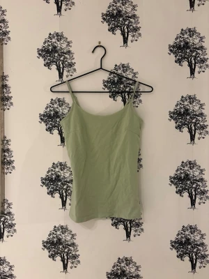 Ljusgrön linnetopp med smala band - Snygg ljusgrön linnetopp med tunna axelband och enkel, rak passform. Perfekt till sommaren och lätt att matcha med olika stilar. Materialet känns mjukt och svalt mot huden.