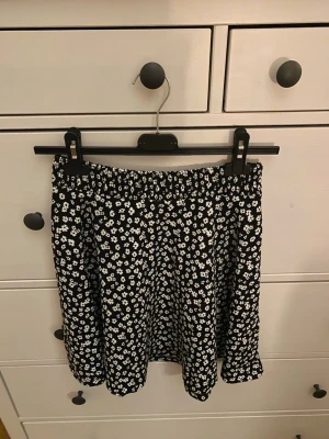 Svart blommig kortkjol - Säljer en svart kortkjol med vita små blommor. Från lager i strl xs/s