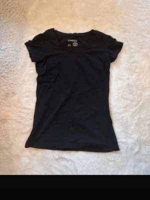 Svart t-shirt från Lindex - En enkel svart t-shirt från Lindex med korta ärmar och rund hals. Perfekt basplagg i garderoben och lätt att matcha till olika stilar. 