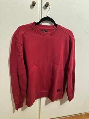 Röd sweatshirt från Lee - Snygg röd sweatshirt från Lee med klassisk rund halsringning och ribbade muddar vid ärmslut och nederkant. Tröjan har en relaxed fit och är tillverkad i mjukt bomullsmaterial. 