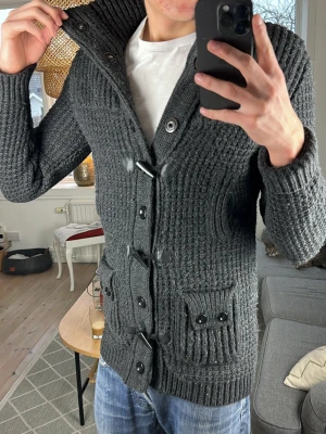 Cardigan mörkgrå  - Riktigt trendig och snygg, perfekt nu i vinter! Mått: A:50 B:42 C:42 D:72 (cm)  Nopprig annars bra skick! Skriv vid fundering😊🙏