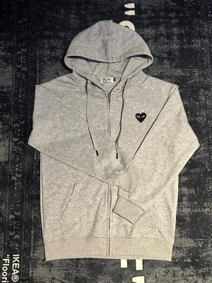 Grå hoodie från CDG storlek M - OBSERVERA HÅLET‼️‼️ tröjan är HELT felfri förutom det lilla hålet!! Väldigt väldigt enkelt att fixa om du har nål och tråd, tyvärr har jag inte tid att fixa. 