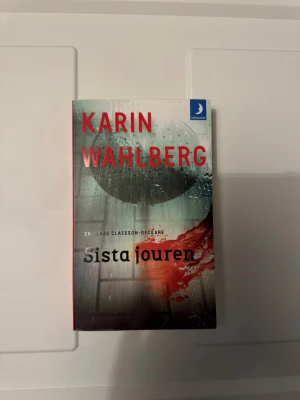 Sista jouren av Karin Wahlberg - Säljer boken 'Sista jouren' av Karin Wahlberg, en spännande deckare i pocketformat. Omslaget har en dramatisk design med rött och grått, och boken ingår i serien om Claes Claesson. Perfekt för dig som gillar kriminalromaner och svenska deckare.