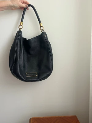 Svart handväska från Marc by Marc Jacobs - Stilren svart handväska från Marc by Marc Jacobs i mjukt skinn med guldfärgade metalldetaljer. Väskan är i gott skick