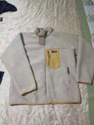 Beige teddyjacka från Patagonia - Mysig beige teddyjacka från Patagonia med gul detaljficka på bröstet och dragkedja framtill. Jackan har långa ärmar, gul kant vid ärmslut och nederkant samt en bröstficka med dragkedja. Perfekt för kalla dagar och riktigt skön att bära.