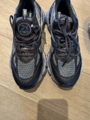 Svarta och grå sneakers från Axel Arigato - Snygga sneakers från Axel Arigato i svart och grå mesh med detaljer i syntet och skinn. Skorna har rund tå, snörning och en chunky platt sula i grått. Perfekta för dig som gillar streetwear och sportig stil.