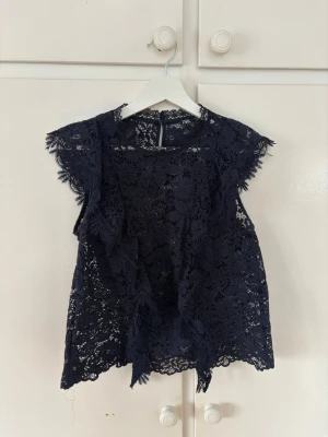 Mörkblå spetsblus från Zara - Säljer en trendig mörkblå blus från Zara i spets med volangdetaljer längs ärmar. Blusen är ärmlös och har en rund halsringning. Storlek S🩷