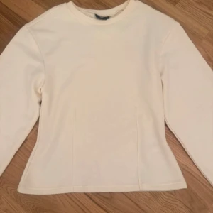 Vit långärmad tröja med rund hals - Säljer en enkel och stilren vit långärmad tröja med rund hals. Tröjan har en lätt figurnära passform och är gjord i ett mjukt material som känns skönt mot huden. Perfekt att matcha med jeans eller kjol för en clean look. Beige vit