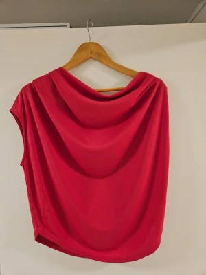 Röd ärmlös topp med draperad hals - Snygg röd topp med draperad halsringning och ärmlös design. Perfekt för dig som vill ha en enkel men ändå stilren look. Tillverkad i mjukt material som känns skönt mot huden och har en loose passform.