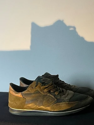 Philippe model sneakers - Snygga sneakers i mörkbrunt mocka och skinn med klassisk låg profil och rund tå. Skorna har snörning och en diskret detalj på sidan. Perfekta för dig som gillar stilrena och tidlösa sneakers.