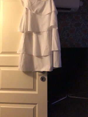 Vit volangklänning från Gina Tricot - Supersöt vit klänning från Gina Tricot med flera lager volanger som ger en flowy och lekfull look. Klänningen är kort och ärmlös, perfekt för varma dagar eller sommarens alla tillfällen. Tillverkad i ett mjukt och lätt material.