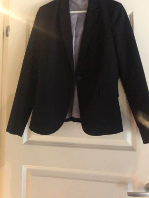 Svart kavaj från Vero Moda - Klassisk svart kavaj från Vero Moda med enkelknäppning och figurnära passform. Fodret har diskreta små prickar för en snygg detalj. Perfekt till både jeans och kostymbyxor.