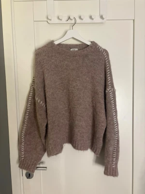 Beige stickad tröja med vita detaljer - Mysig beige stickad tröja från Jdy med avslappnad passform och vita dekorativa sömmar längs ärmarna. Tröjan har rund halsringning, långa ärmar och ribbade muddar. Perfekt för lager på lager och en chill look.