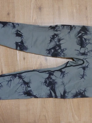 Grå tie-dye leggings med svart mönster - Snygga grå leggings med svart tie-dye mönster. De har hög midja och är tillverkade i ett stretchigt syntetmaterial som sitter tight och bekvämt. De har en scrunch i rumpan som syns lite. 