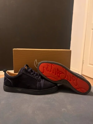 Mörkblå sneakers från Christian Louboutin - ( TAR IMOT BYTEN) Snygga mörkblå sneakers från Christian Louboutin i mocka med klassisk röd sula och rund tå. Skorna har snörning och en stilren design som passar perfekt till streetwear eller en mer uppklädd look.