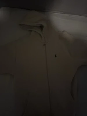 Beige hoodie från Polo Ralph Lauren - Snygg beige hoodie från Polo Ralph Lauren med dragkedja och klassisk logga broderad på bröstet. Hoodien har huva och är tillverkad i mjukt material som känns skönt mot huden. Perfekt för en avslappnad och stilren look.