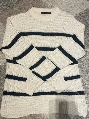 Vit och svart randig stickad tröja 157 - Säljer en vit stickad tröja från 157 i storlek M med svarta horisontella ränder. Tröjan har rund hals, grovstickad struktur och långa ärmar med breda muddar. Perfekt för dig som gillar klassisk och chill stil.