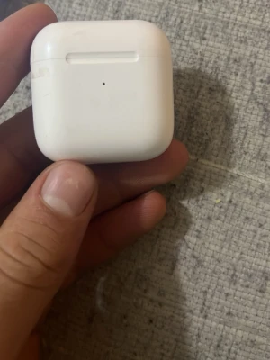 AirPods 2 - Apple AirPods 2 med laddningsetui. Trådlösa hörlurar med enkel anslutning till iPhone och andra Apple-enheter. Fungerar och laddar som de ska, men viss smuts och slitage syns på hörlurarna och etuiet. Perfekt för dig som vill ha bekväma hörlurar till ett bra pris.