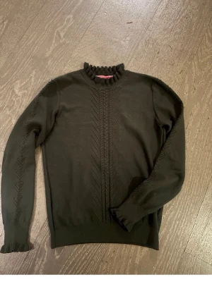 Svart stickad tröja från Bondelid - Svart stickad tröja från Bondelid med snygga detaljer som strukturstickat mönster framtill och på ärmarna. Tröjan har långärmad design, ribbad och volangkantad halsringning samt muddar. Perfekt för dig som gillar stilrena och unika plagg. Passar även S. Nyskick❤️