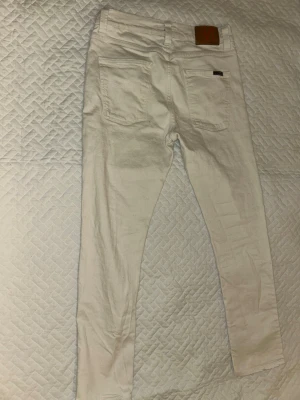 Vita jeans från Nudie Jeans, W31 L30 - 9/10 vita jeans från Nudie Jeans med klassisk femficksdesign och raka ben. Byxorna har metallnitar, knappgylf och Nudie Jeans-lapp bak i brunt läder. 