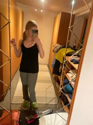 Svart linnetopp med spetsdetaljer - Säljer en svart linnetopp med tunna axelband och v-ringning. Toppen har fina spetsdetaljer längs urringningen och axelbanden, vilket ger en extra touch. Perfekt att styla med jeans eller kjol för en enkel men snygg look.