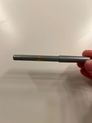 Silvergrå eyelinerpenna - Snygg eyelinerpenna i silvergrå färg med metallic finish. Pennan har ett stilrent grått hölje med gulddetalj och är lätt att applicera för en skarp och glansig linje. Perfekt för att skapa en cool och glittrig look runt ögonen.