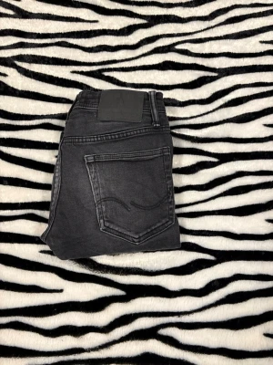 Jack & Jones svarta jeans - Snygga svarta jeans från Jack & Jones med klassisk femficksdesign och metallknappar. Jeansen har en rak passform och är tillverkade i slitstarkt bomullsmaterial med dragkedja i gylfen. Perfekta för dig som gillar en enkel och stilren look. Slim/glenn hör av dig vid minsta fundering 😌