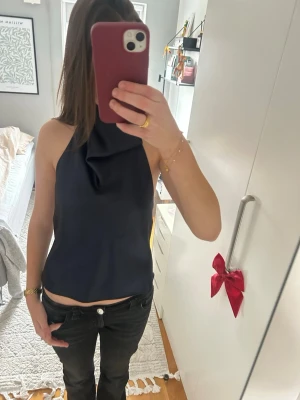 Svart halterneck linnetopp i satin - Säljer en jättefin mörkblå halterneck linnetopp i satin med snygg öppen rygg. Toppen är ärmlös och har en croppad passform som ger en trendig look. En Tråd har gått upp snett över hela tröjan men man ser det knappast när man har på den. Skriv om tydligare bild!