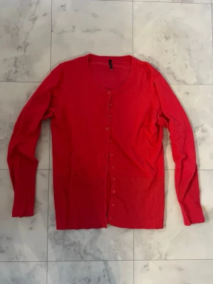 Röd kofta från Soyaconcept - Snygg röd kofta från Soyaconcept med rund hals och långa ärmar. Koftan har knappar hela vägen framtill och ribbade muddar vid nederkant och ärmslut. Perfekt att slänga över en t-shirt eller linne för en chill look.