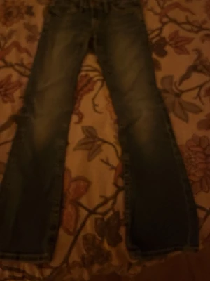 Blå bootcut jeans med detaljer - Snygga blå jeans med bootcut-snitt och klassisk femficksdesign. Jeansen har slitningar framtill och coola bakfickor med dekorativa sömmar och guldfärgade knappar. Perfekt för dig som gillar en avslappnad och trendig look.Dom är dock lite sönder som jag visar på en bild men är väldigt lätt att sy❤️