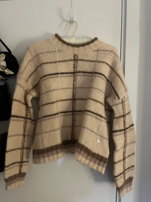Beige rutig stickad tröja Mos Mosh - Säljer en stickad tröja från Mos Mosh i beige med brunt och rosa/lila rutmönster. Tröjan är i bra skick men är lite nopprig (jag tar bort det innan jag skickar tröjan) 