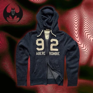 Blå hoodie Abercrombie & Fitch med dragkedja  - Blå hoodie med dragkedja med vit markerad text ’92 Abercrombie’ | lite sliten, titta bilder | fint skick | size L / XL | Längd: 72cm Arm: 74cm Axelbredd: 48cm | Modell 162cm, 60kg 