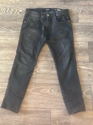 Replay Anbass svarta jeans - Svarta jeans från Replay, modell Anbass, i storlek 32. Klassisk femficksdesign med smal passform och raka ben. Jeansen har en mörk tvätt och är tillverkade i mjukt jeansmaterial med stretch för extra komfort. Perfekta för en avslappnad och stilren look.