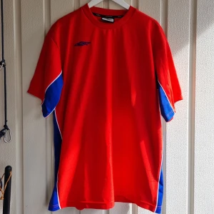 Röd t-shirt från Umbro - Snygg tröja från Umbro med blå och vita detaljer längs sidorna. Det är farsans gamla kläder som hittats. Priset kan diskuteras 
